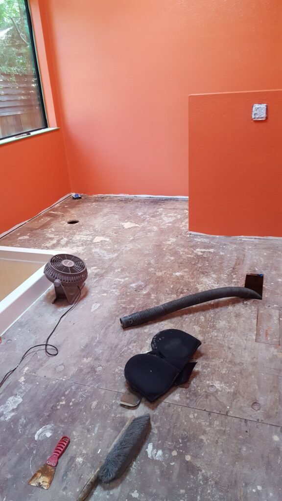 Exposed plywood bathroom subfloor beside a white shower base before membrane and tile installation in Mill Valley.