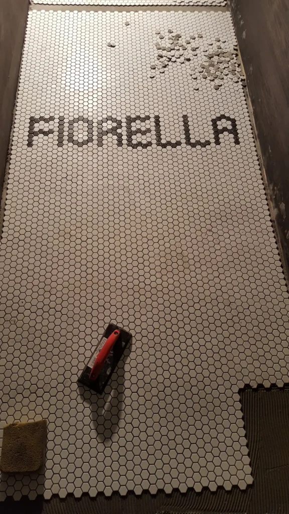 Custom FIORELLA restaurant name spelled out in dark hexagon tiles surrounded by white hexagon mosaic flooring in San Francisco.