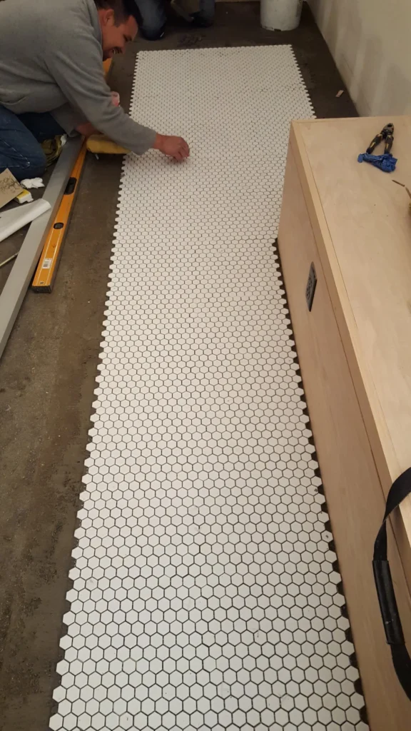 Tile installer positioning white hexagon mosaic floor tile sheets during the Fiorella Restaurant project.