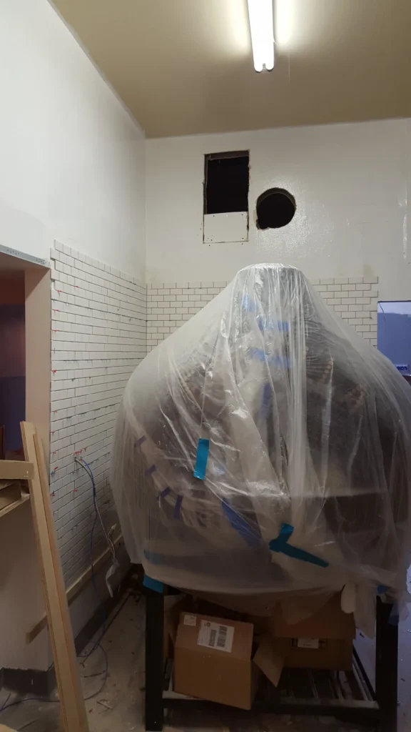 White subway tile being installed on restaurant kitchen walls with commercial equipment protected during construction.