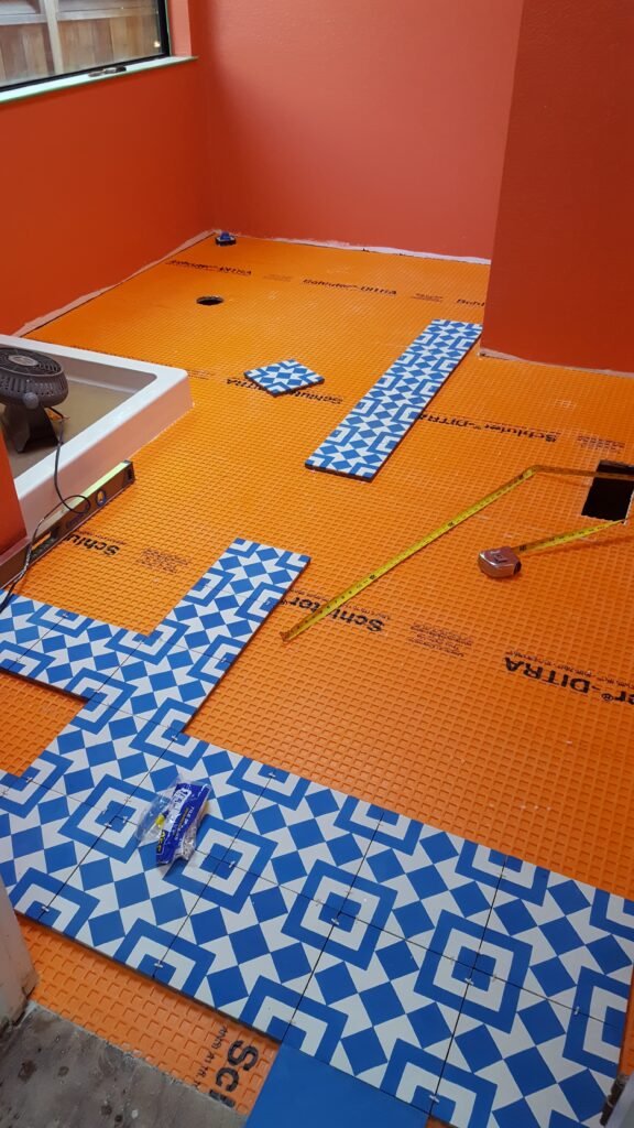 Overview of a Mill Valley bathroom floor covered in Schluter-DITRA membrane, with blue-and-white geometric tiles dry-laid to plan the pattern.