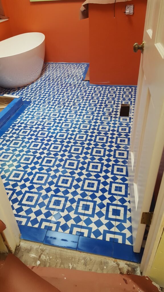 Installed blue-and-white geometric bathroom floor tile with a solid blue border at the doorway, freestanding tub beyond, in Mill Valley.