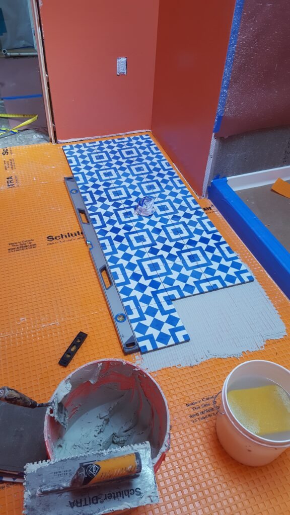 Setting blue-and-white geometric floor tile in thinset over Schluter-DITRA in a Mill Valley bathroom, with a level, trowel and mortar bucket.
